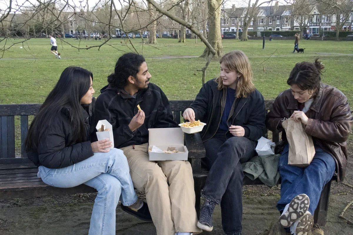 Friends sharing chips on a bench in a London park